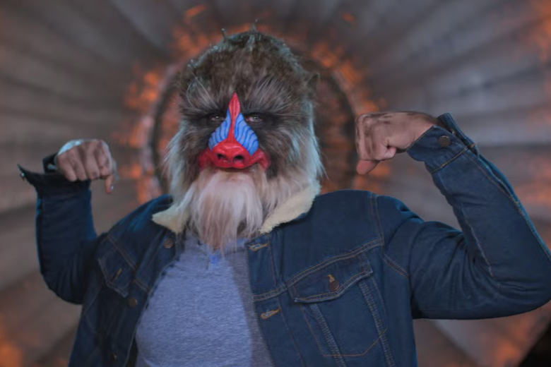 A man in a jean jacket with a Mandrill mask on his head. 