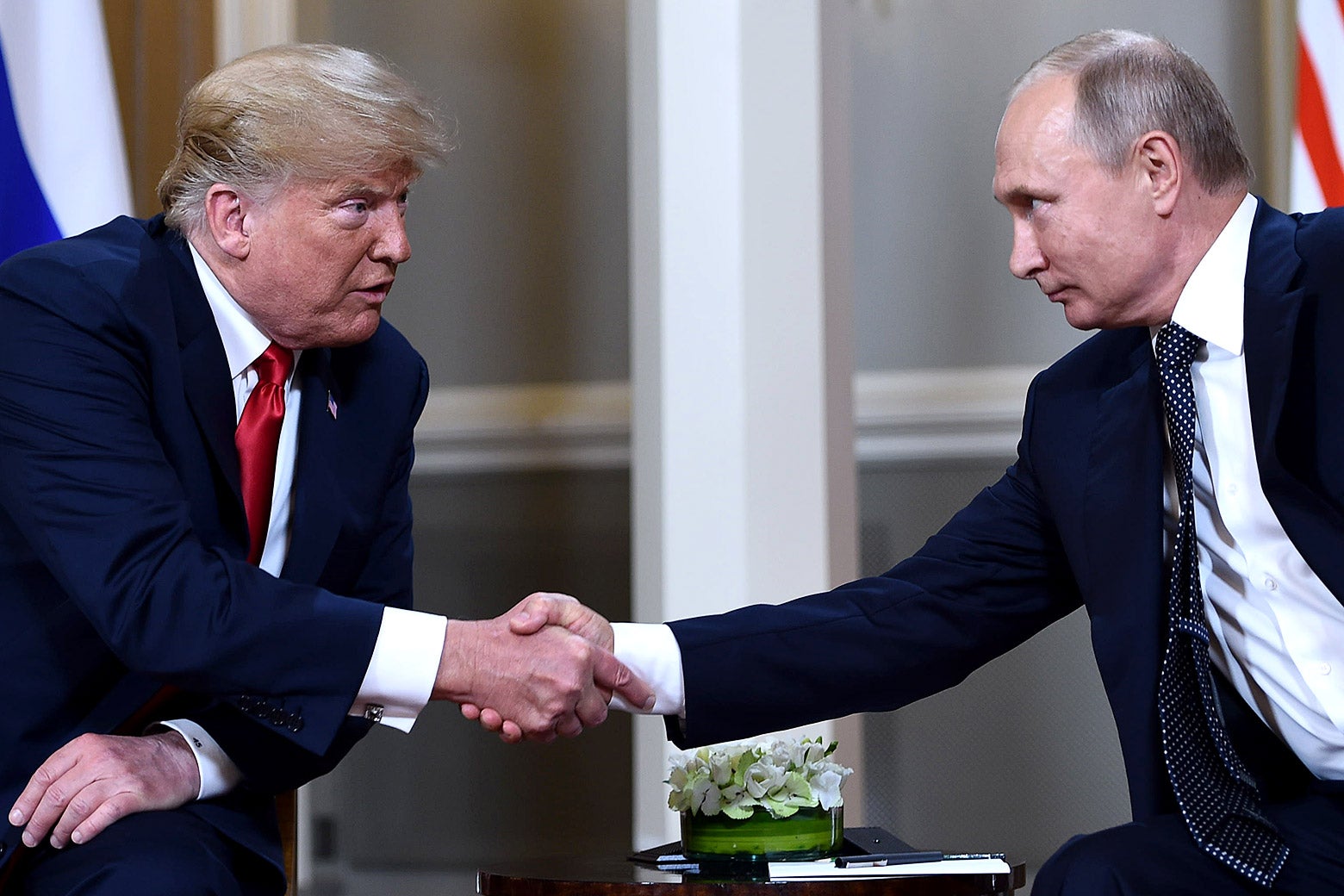 Donald Trump and Vladimir Putin, seated, shake hands.